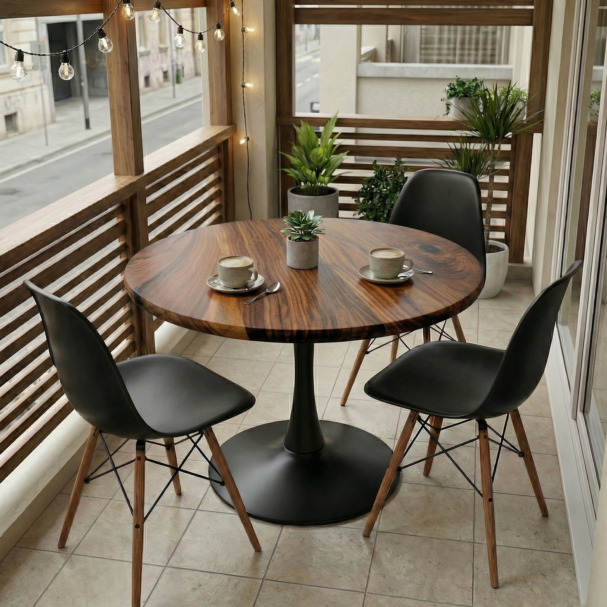 Round wooden table with black chairs on a balcony with plants and string lights.