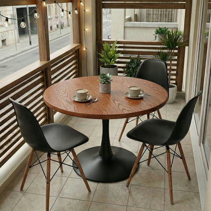 Round wooden table with black chairs on a balcony with plants and string lights.